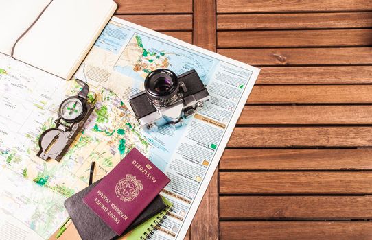 Top view of compass, photocamera, block notes, passport and map on a wooden table