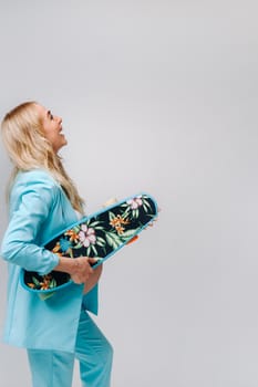 a pregnant girl in turquoise clothes with a skateboard in her hands on a gray background.