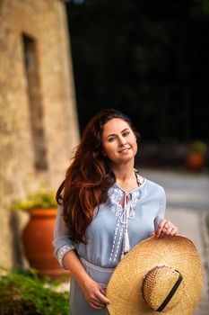 A girl in a dress and hat walks in the afternoon in an Italian town in Tuscany.