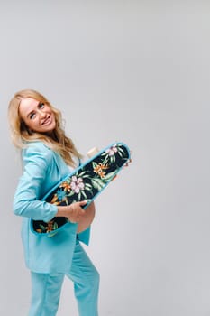 a pregnant girl in turquoise clothes with a skateboard in her hands on a gray background.