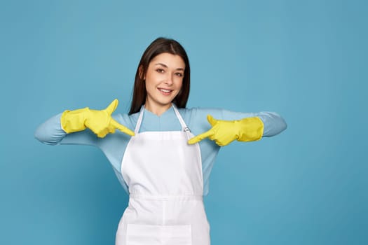 happy caucasian woman in yellow rubber gloves pointing oneself with fingers on blue background. cleaning