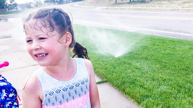 Little girl playing in sprinkles on the hot summer day.