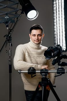 Professional handsome photographer with digital camera on tripod on gray background with lighting equipment