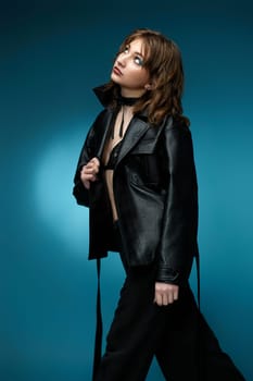 young stylish woman posing in black leather jacket and pants on blue background.