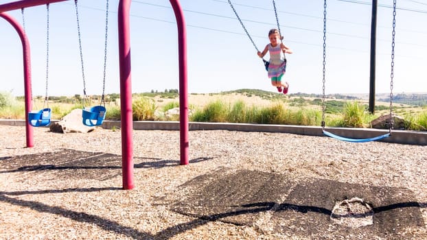 Little girl playing on swings at children's playground in suburbs.