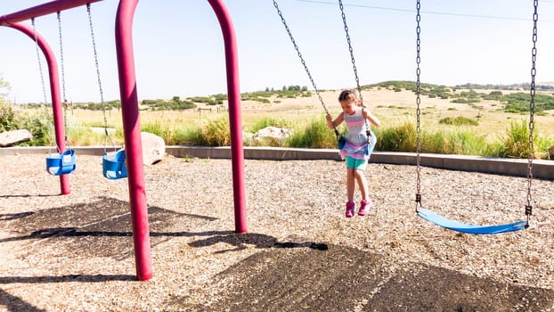 Little girl playing on swings at children's playground in suburbs.