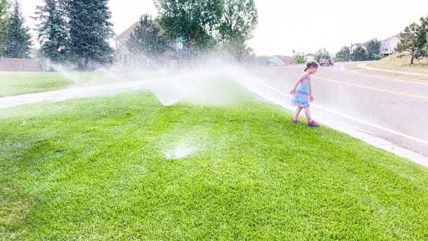 Little girl playing in sprinkles on the hot summer day.