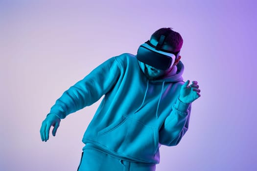 man in sweatshirt using virtual reality glasses and playing video games on blue background. Neon lighting