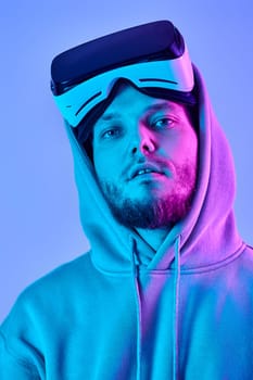 man in sweatshirt using virtual reality glasses and playing video games on blue background. Neon lighting