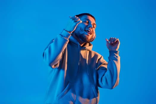 handsome man listening to music with wireless headphones on blue background. Neon lighting