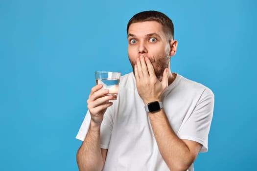 handsome surprised handsome man with drinking glass of water on blue background
