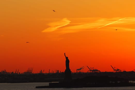 Silhouette of Statue of Liberty and Liberty Island in New York against an orange sunset sky