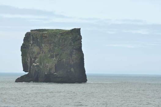 Scenic view of Icelandic peninsula with waves hitting huge black rock at overcast Dyrholaey Cape