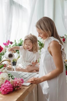 A little blonde girl with her mom on a kitchen countertop decorated with peonies. The concept of the relationship between mother and daughter. Spring atmosphere.