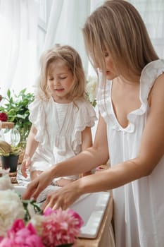 A little blonde girl with her mom on a kitchen countertop decorated with peonies. The concept of the relationship between mother and daughter. Spring atmosphere.