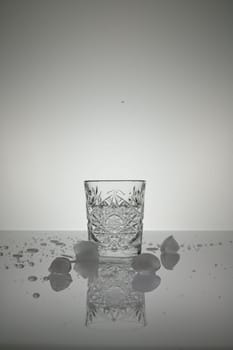 Vertical shot of crystal water glass, ice cubes and waterdrops around, on a white shiny surface