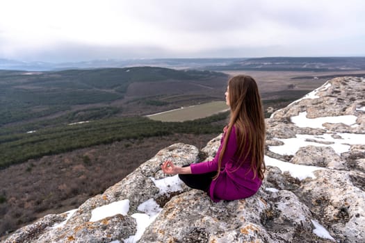 A beautiful woman sits in a lotus position on a high place with an amazing view of the mountains and the gorge practicing yoga meditation Kundalini energy thinking intuition prana. Loneliness harmony mental freedom concept.