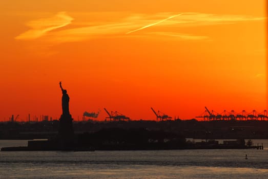 Silhouette of Statue of Liberty and Liberty Island in New York against an orange sunset sky