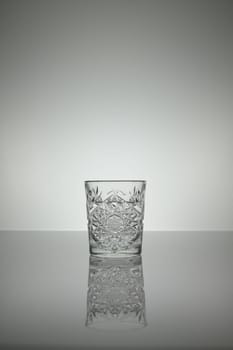 Crystal water glass reflecting on a gray surface with white background