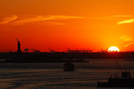 Silhouette of Statue of Liberty and Liberty Island in New York against an orange sunset sky