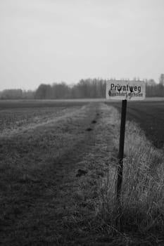 Vertical greyscale shot of a sign showing a private way on a field in Meerbusch, Germany