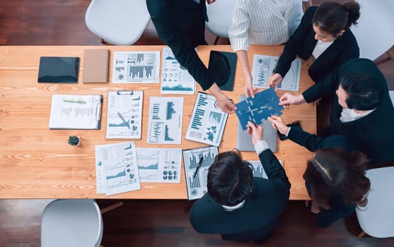 Top view businesspeople and colleagues in formal wear putting jigsaw puzzles together over meeting table with financial report papers in harmony office for team building concept.