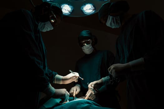 Surgical team performing surgery to patient in sterile operating room. In a surgery room lit by a lamp, a professional and confident surgical team provides medical care to an unconscious patient.