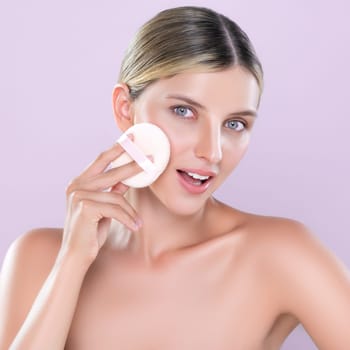 Alluring beautiful female model applying powder puff for facial makeup concept. Portrait of flawless perfect cosmetic skin woman put powder foundation on her face in pink isolated background.