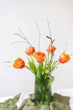 A very beautiful spring bouquet in a green vase stands on a table on a linen tablecloth, orange peony tulips. Mother's Day, March 8, Valentine's Day