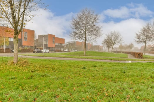 a grassy field with trees and buildings in the background on a foggy day, autumn or early fall time