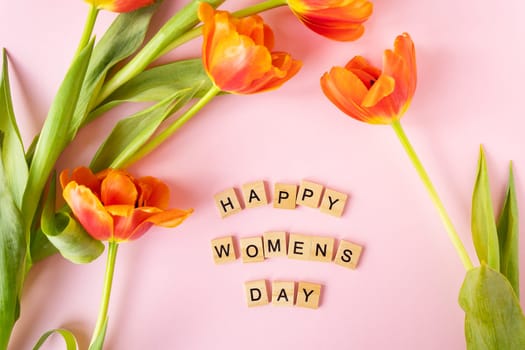 March 8, postcard. Happy Women's Day text sign with orange tulips on pink background. Stylish flat lay with flowers and text, greeting card