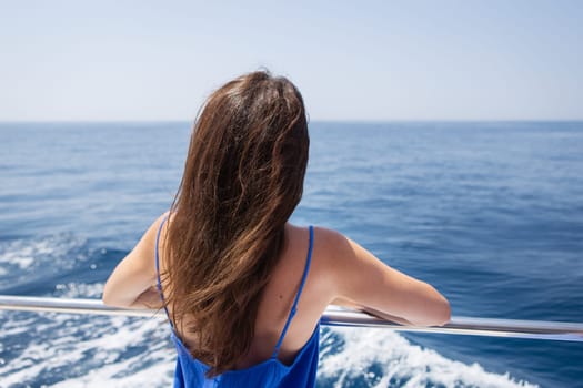 Young beautiful brunette girl sits with her back on a yacht against the backdrop of a beautiful blue sea or ocean
