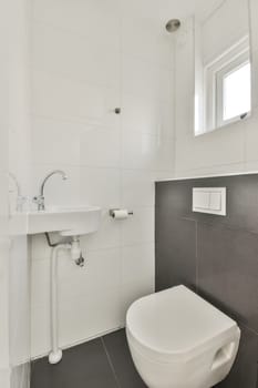 a white toilet and sink in a small bathroom with black tiles on the floor, there is a window above it
