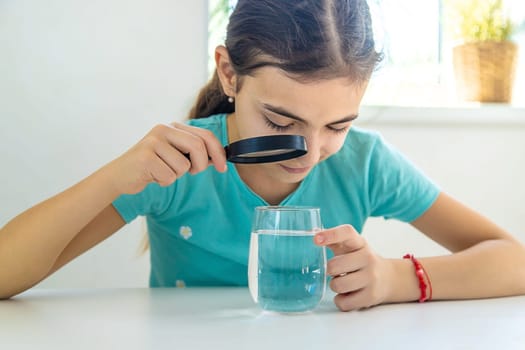 The child examines the water under a magnifying glass. Selective focus. Kid.