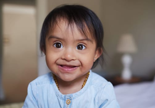 Happy, portrait smile and Down syndrome baby relaxing on a bed in happiness at home. Cheerful little child with genetic disorder or disability smiling in bedroom for cute childhood and development.