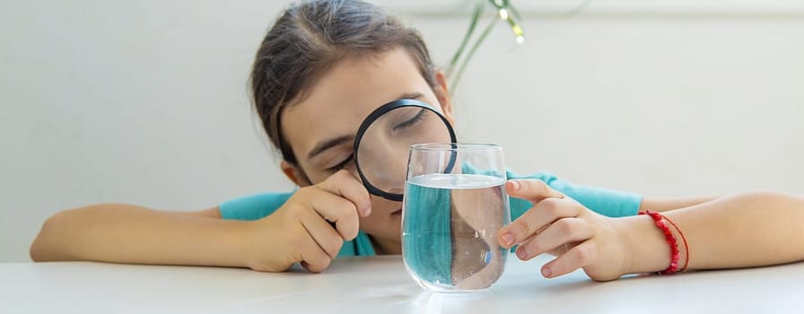 The child examines the water under a magnifying glass. Selective focus. Kid.