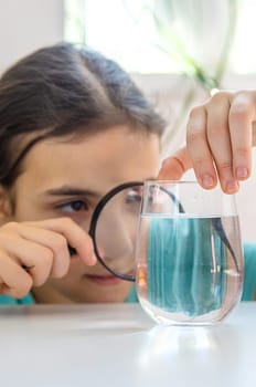 The child examines the water under a magnifying glass. Selective focus. Kid.