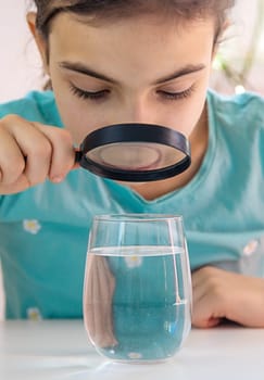 The child examines the water under a magnifying glass. Selective focus. Kid.