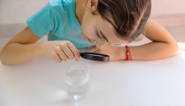 The child examines the water under a magnifying glass. Selective focus. Kid.