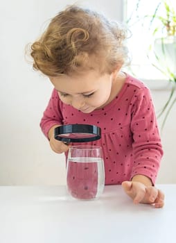 The child examines the water under a magnifying glass. Selective focus. Kid.