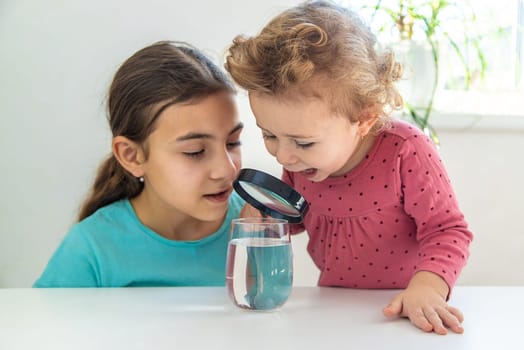 The child examines the water under a magnifying glass. Selective focus. Kid.