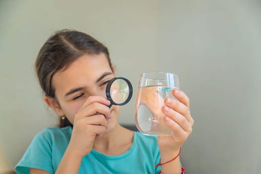 The child examines the water under a magnifying glass. Selective focus. Kid.