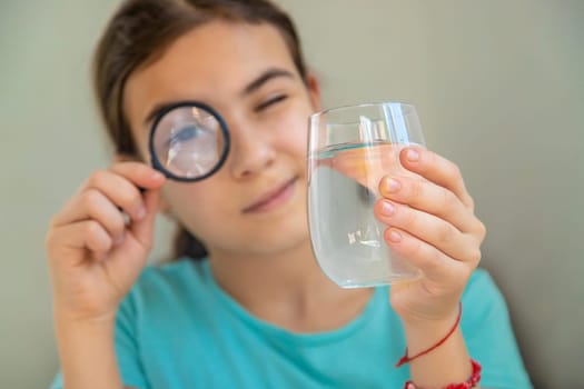 The child examines the water under a magnifying glass. Selective focus. Kid.