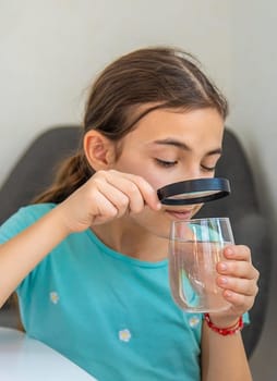 The child examines the water under a magnifying glass. Selective focus. Kid.