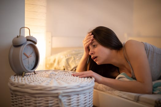 A disgruntled young girl looks at the ringing alarm clock. Bedroom in bright colors.