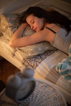 The brunette hugs her pillow in her sleep. A white alarm clock stands on the nightstand.