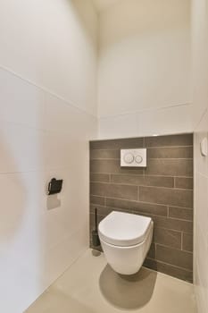 a toilet in the corner of a white bathroom with gray tiles on the walls and floor, there is a black hand towel hanging
