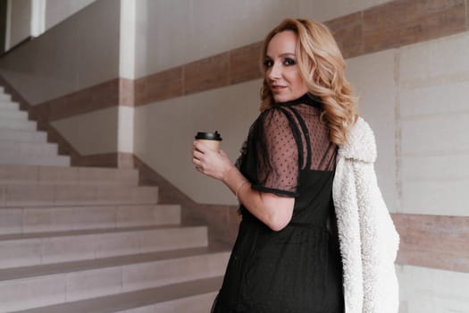 Portrait of a beautiful smiling blonde. She's walking up the stairs, coffee in hand. The Concept Of Urban Life