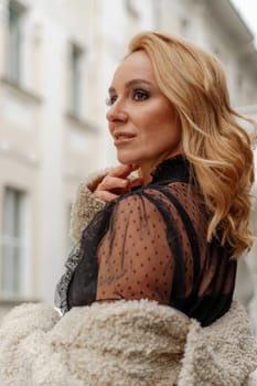 Profile of a beautiful blonde. She looks away and smiles. She is dressed in a black lace dress and a milky faux fur coat