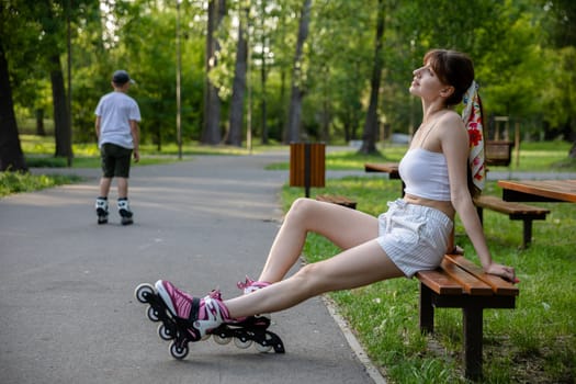 Roller skating in a city park. Active spending time on a summer sunny day. Person dressed in summer sportswear in shades of white. In the background the distant figure of a boy riding on roller skates.